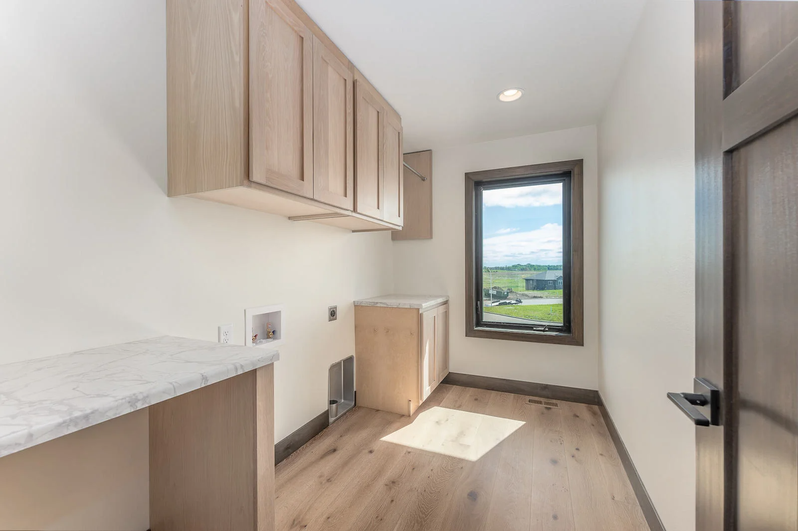 A laundry room with wooden floors , cabinets and a window.