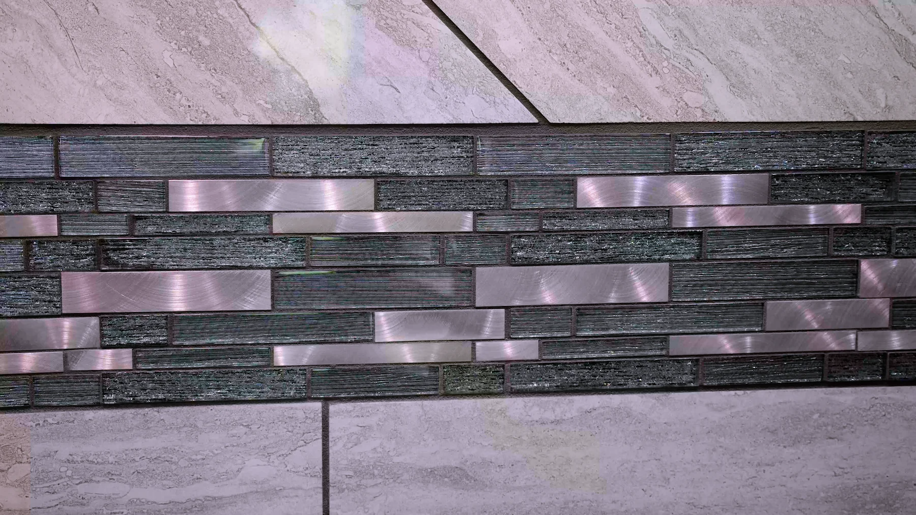 A tile wall with a stainless steel border is sitting on a tiled floor.