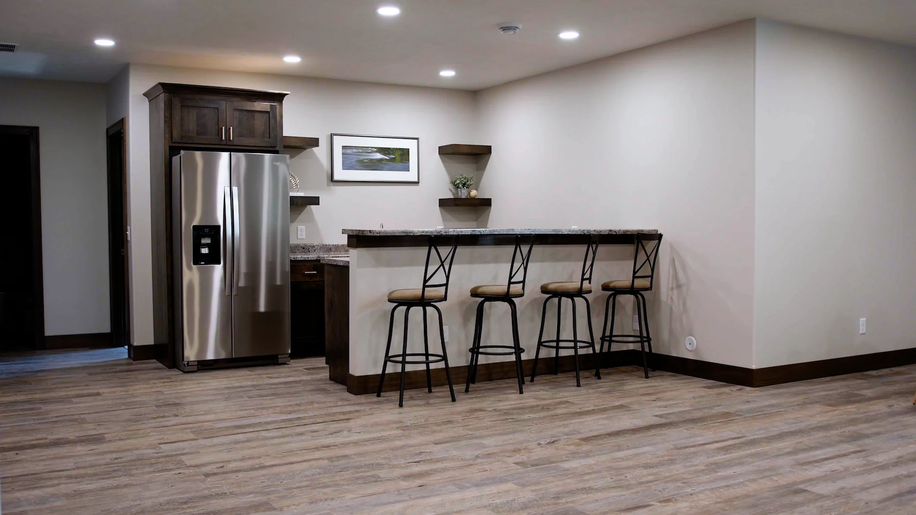 A basement with a bar and stools and a refrigerator.