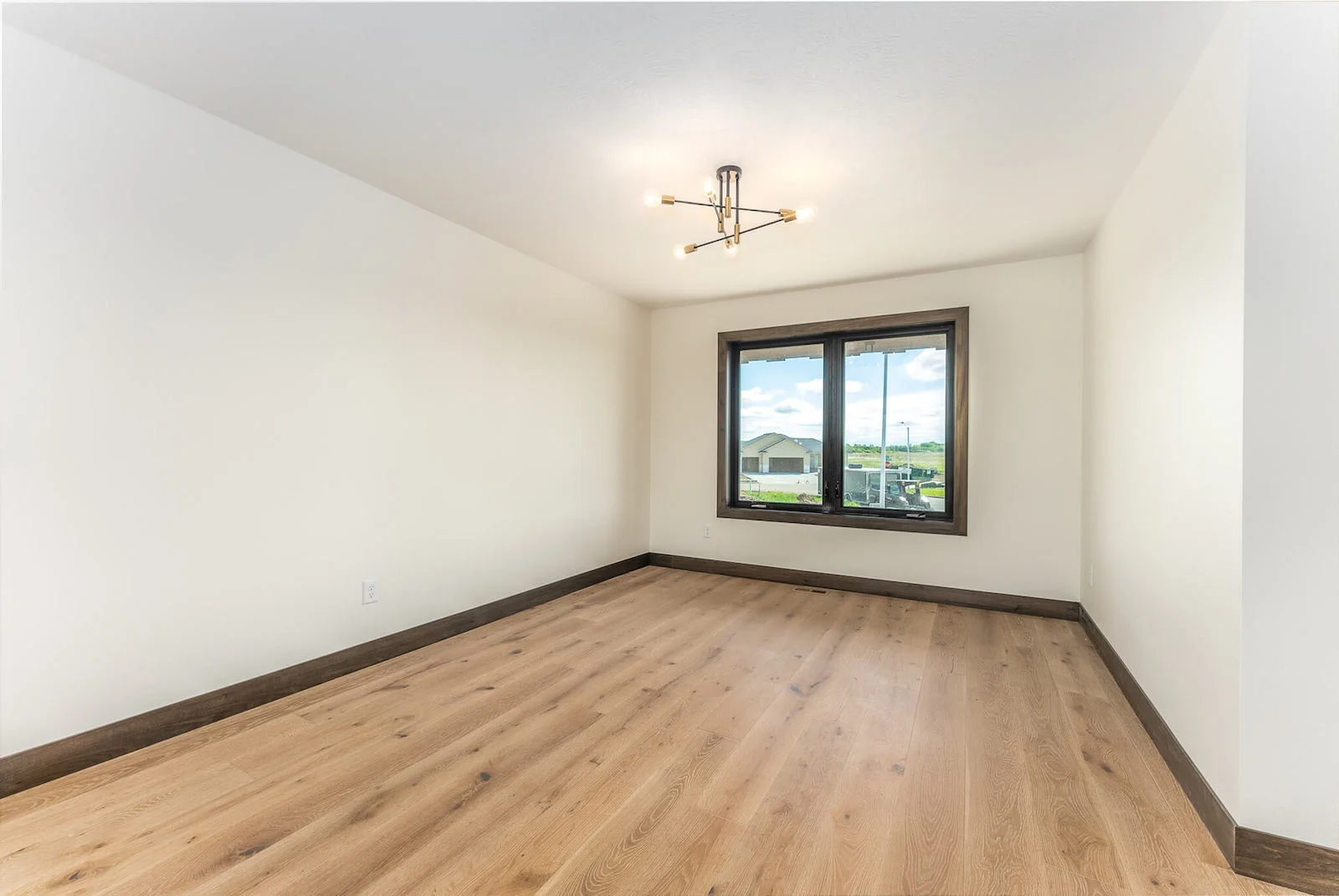 An empty bedroom with hardwood floors and two windows.