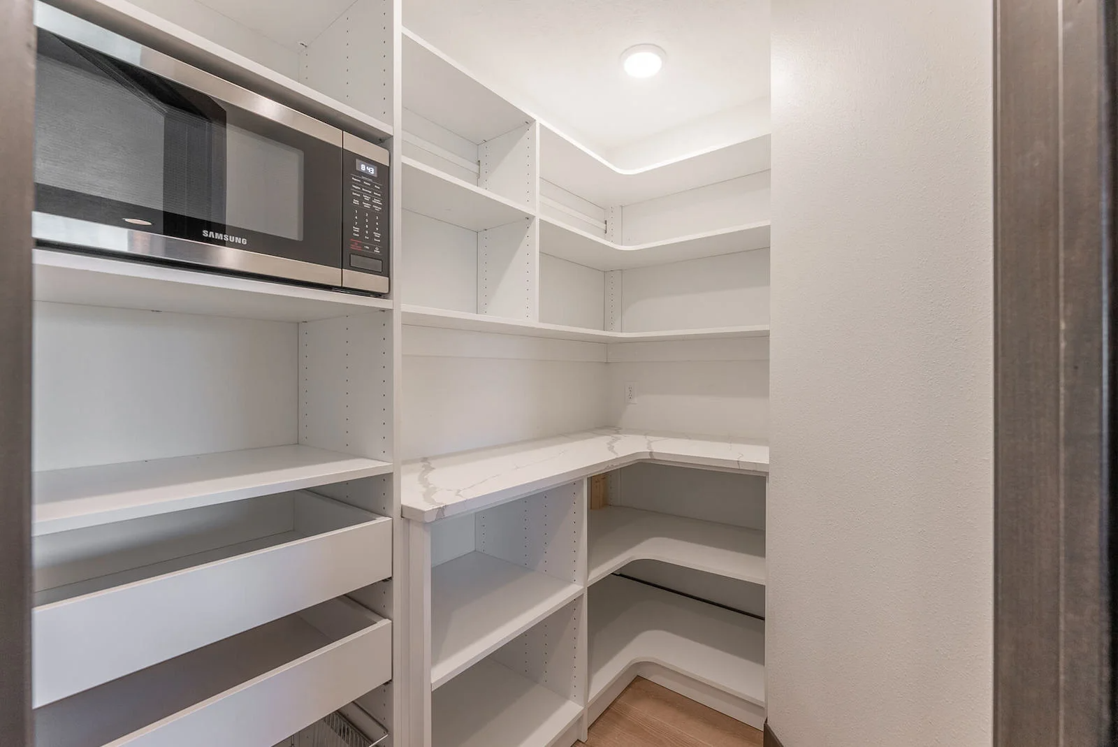 A pantry with shelves , drawers and a microwave.