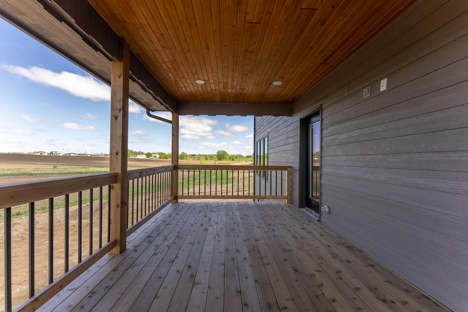 An empty porch with a wooden railing and a view of a field.