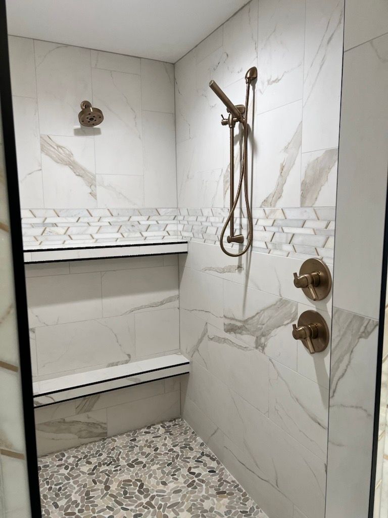 A walk in shower with two shower heads and a bench.