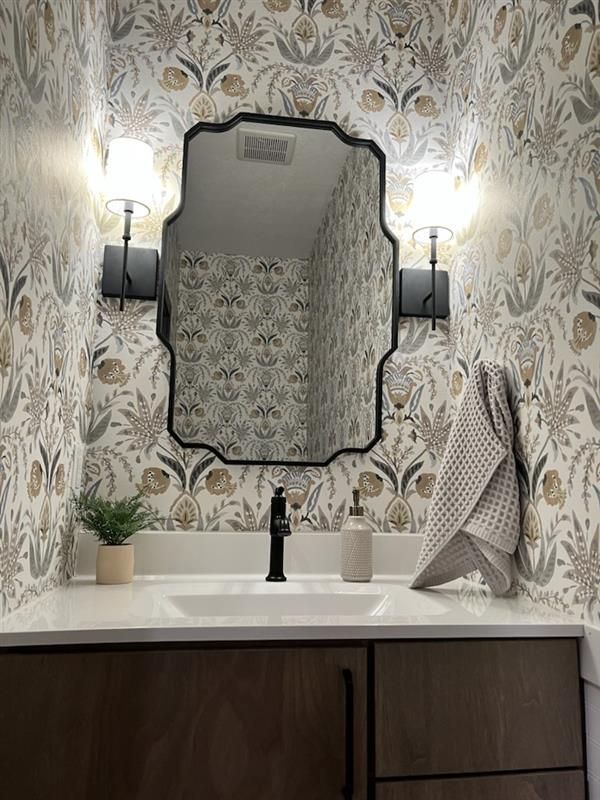 A bathroom with a sink, mirror, and wallpaper.