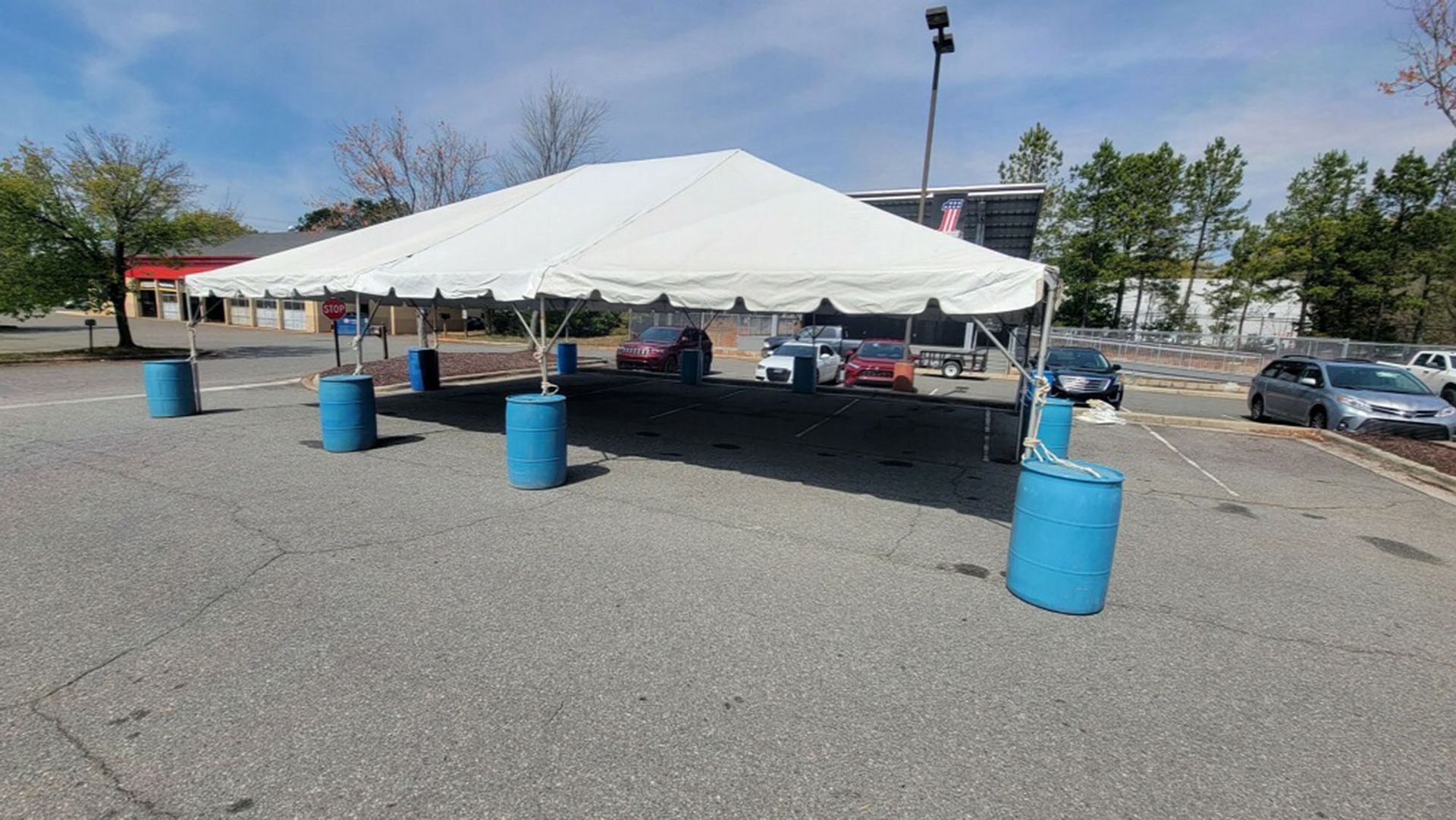 A white tent is sitting in a parking lot next to blue barrels