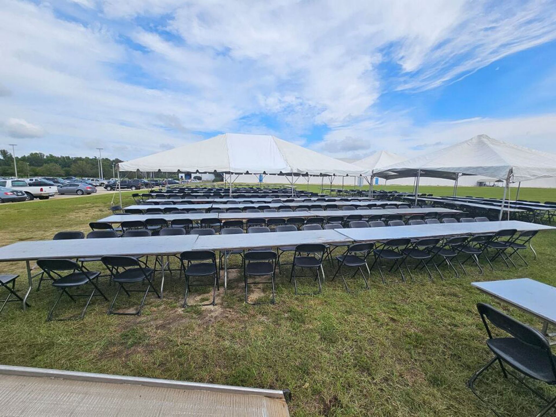A row of folding tables and chairs under a tent in a field
