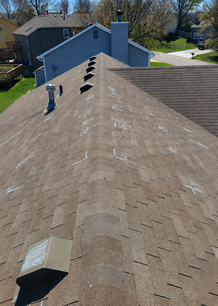 Aerial view of a shingled residential roof with vents and nearby houses in a neighborhood