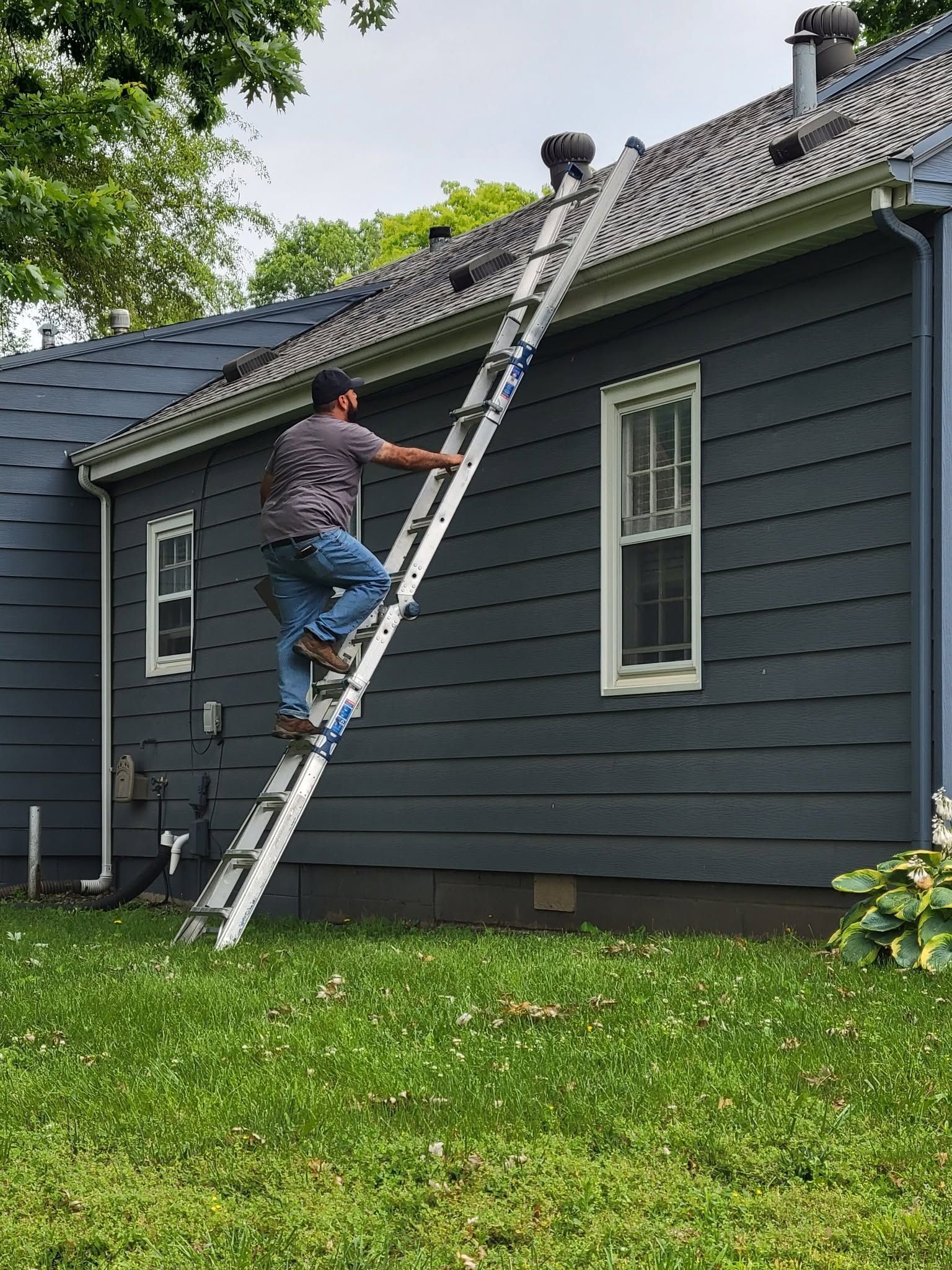 Worker climbs ladder to inspect the roof of a dark gray house