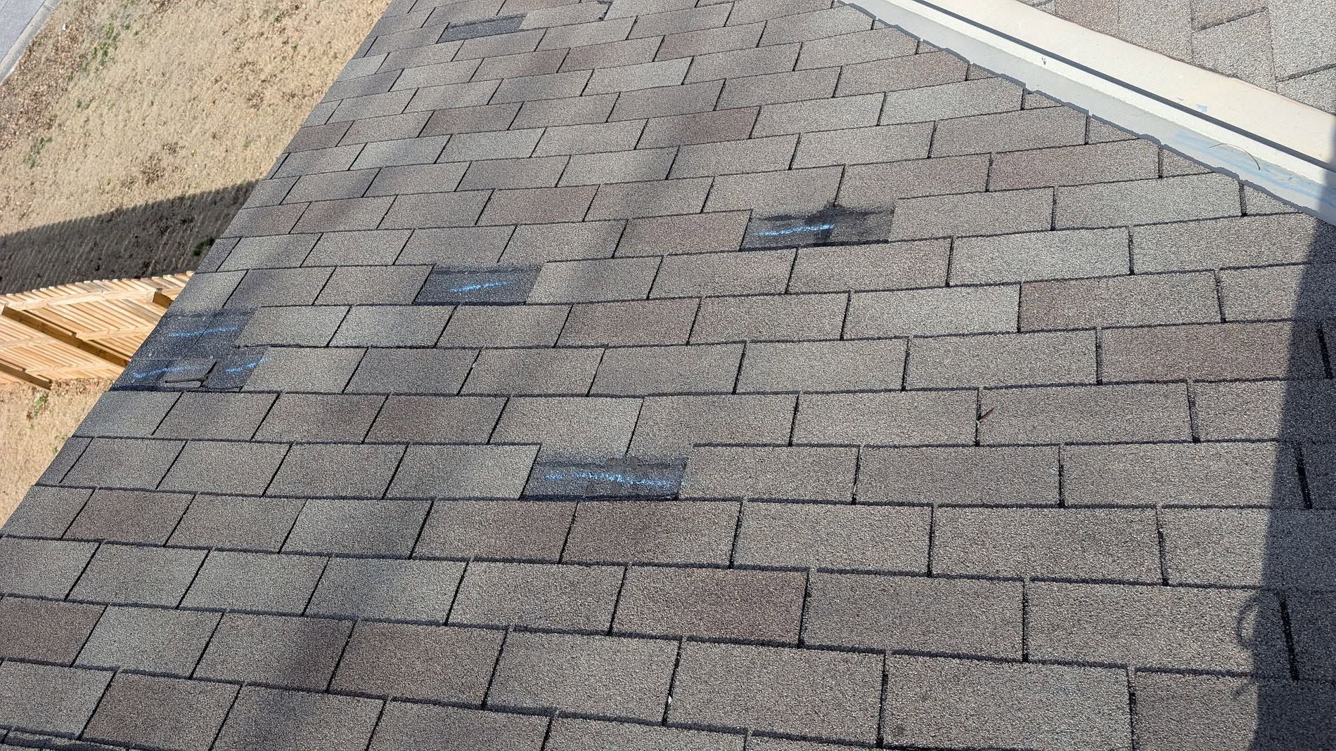 Gray shingle roof with a small damaged patch near the top center, viewed in daylight