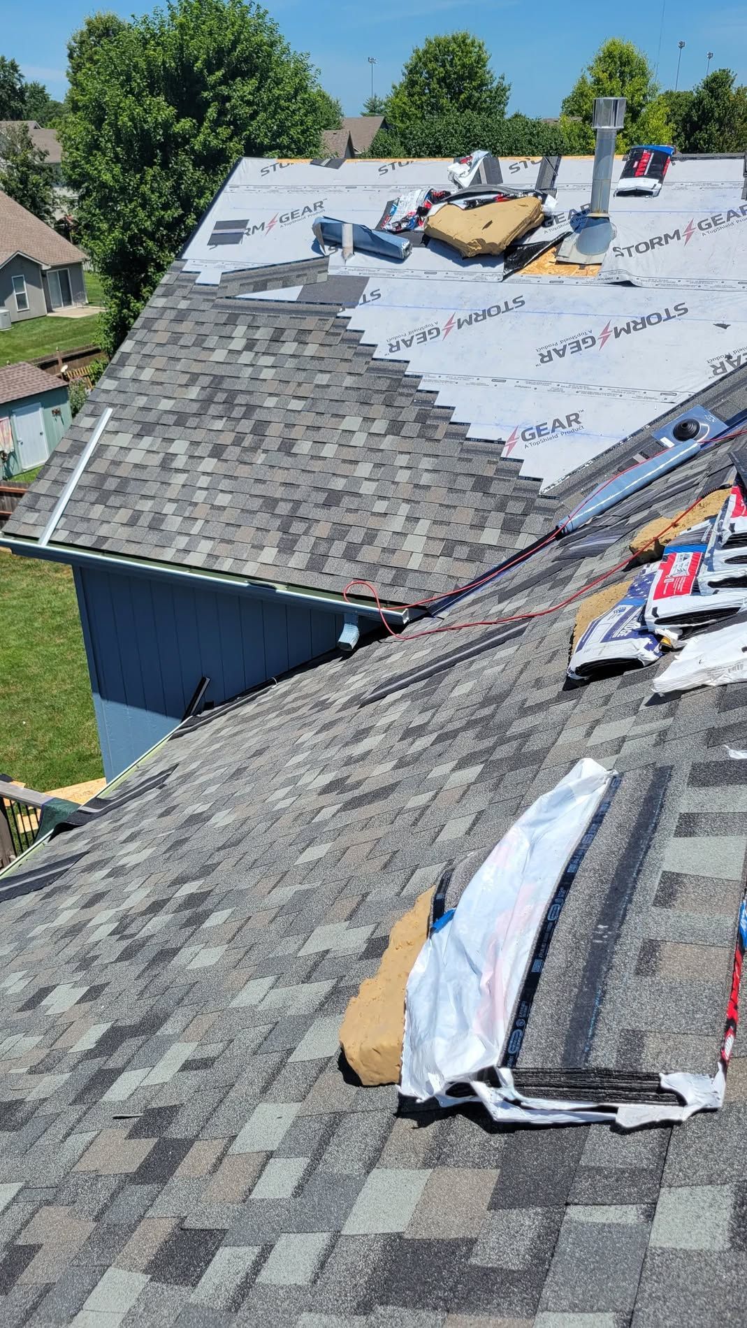 Roof under repair with gray shingles, white underlayment, and construction materials on a sunny day