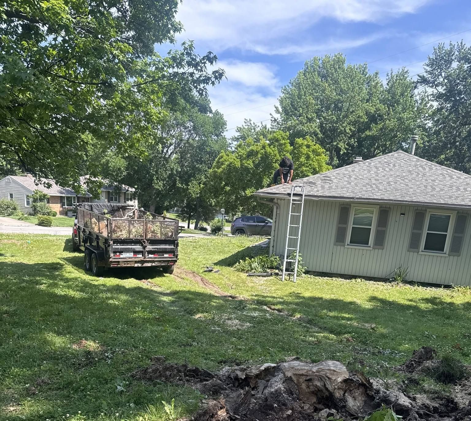 Yard with a truck loaded with debris beside a small white house under trees.