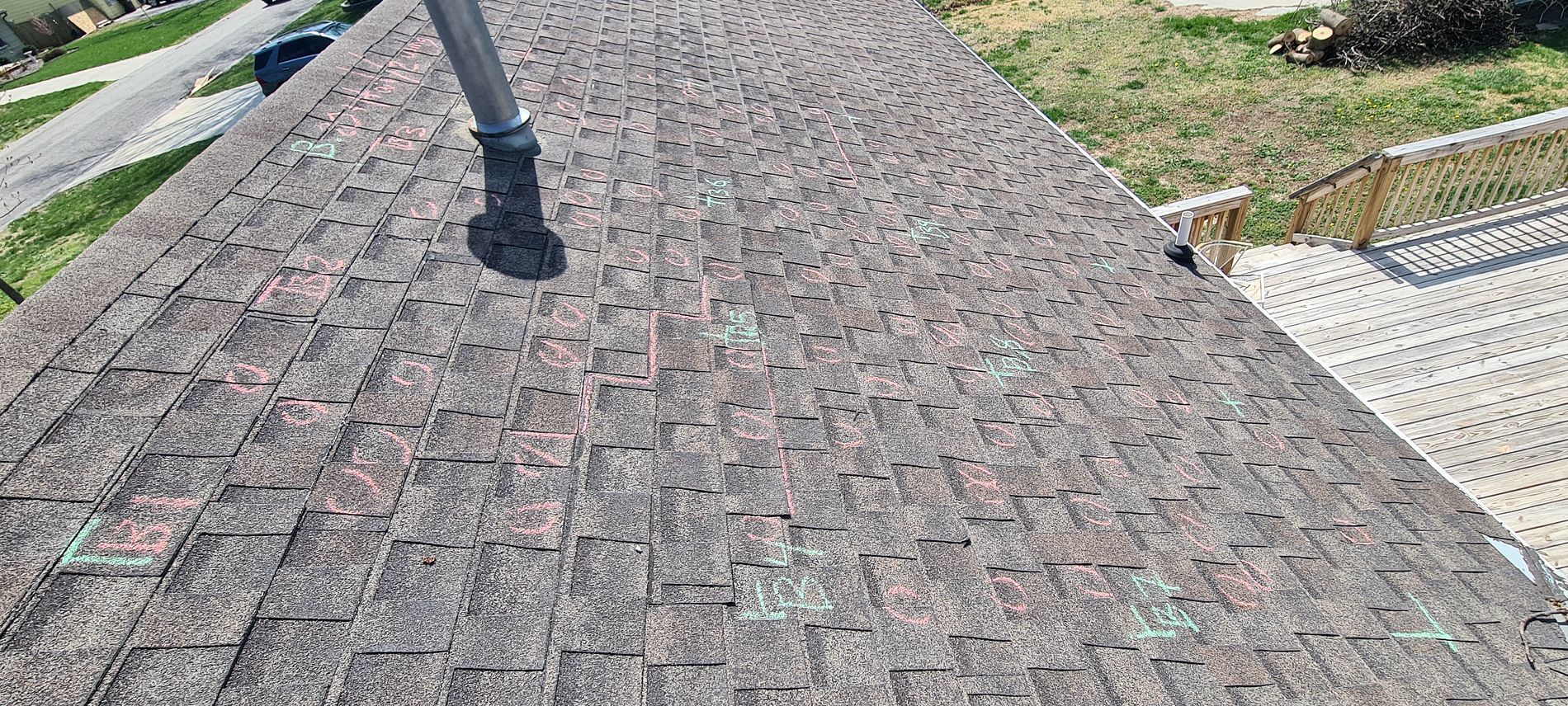 Roof covered in brown asphalt shingles with a vent pipe and a glimpse of yard and walkway below