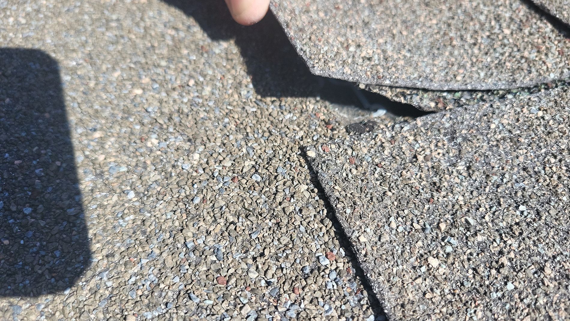 Close-up of cracked asphalt pavement with a hand shadow and a person’s foot at the top edge