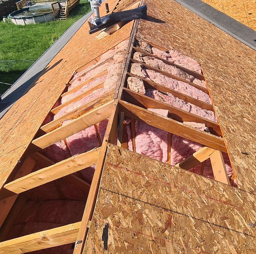 Roof under construction with exposed plywood sheathing, pink insulation, and wooden rafters on a sloped roof.