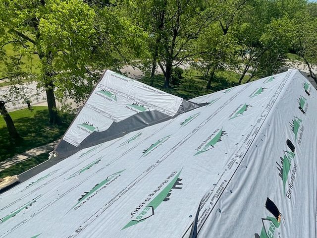 Partially shingled roof with exposed underlayment, surrounded by trees