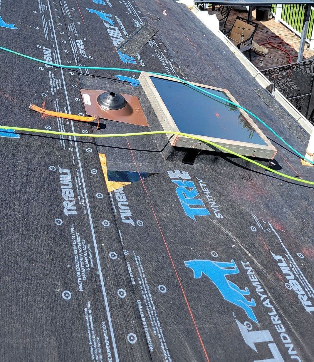 Roof under repair with black underlayment, a vent pipe, and a skylight frame near the ridge.