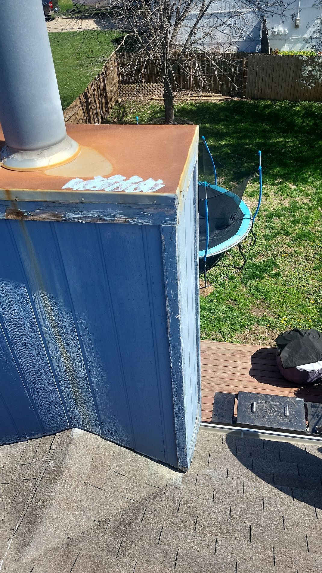 Blue metal cabinet with rusted top beside a concrete walkway, with a hose reel and grass in the yard.