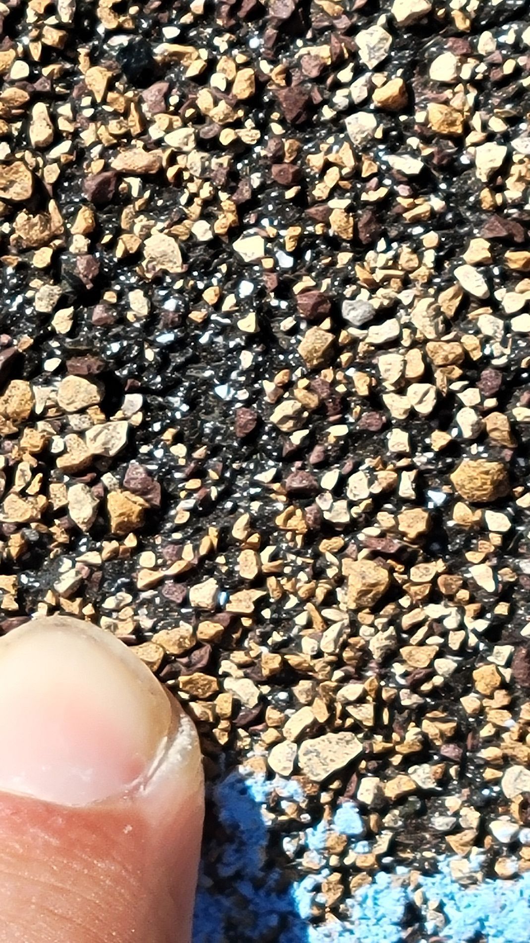 Close-up of coarse gravel asphalt with a fingertip at the bottom left edge.
