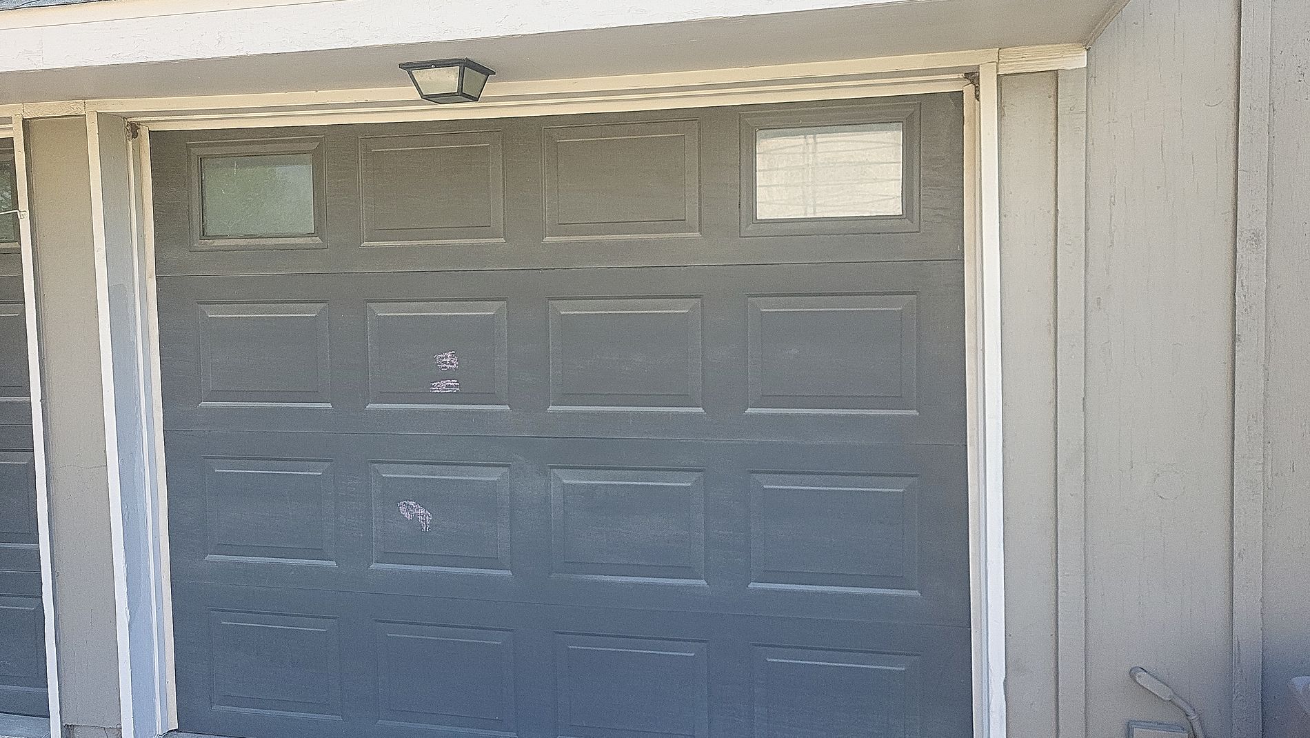 Gray garage door under a white overhang with light beige siding on the right