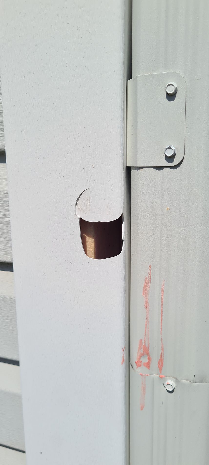Close-up of a white metal door frame with a circular hole exposing copper-colored interior.