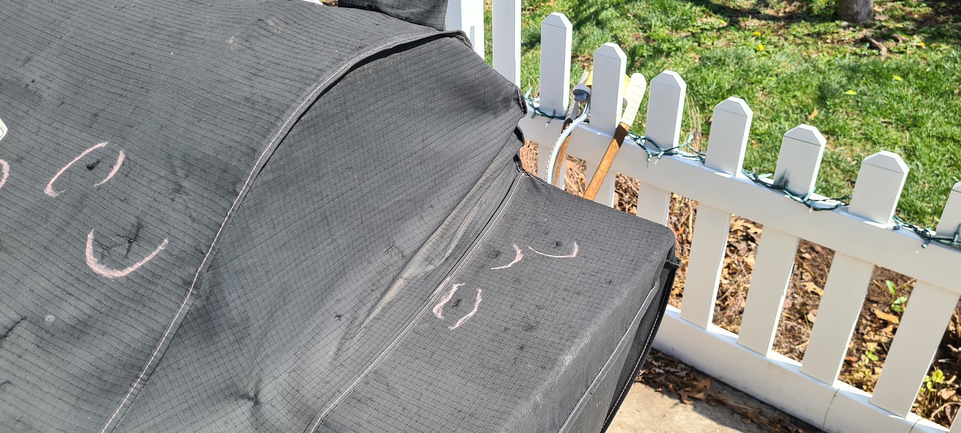 Black outdoor furniture cover with cat scratches beside a white picket fence and grass