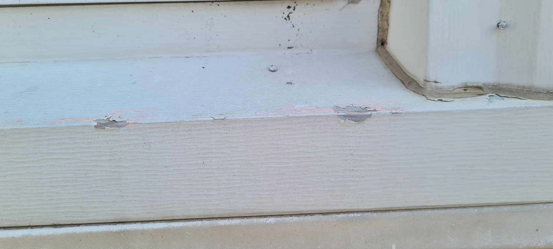 Close-up of a white painted wooden wall and trim with peeling paint and rust stains near a corner