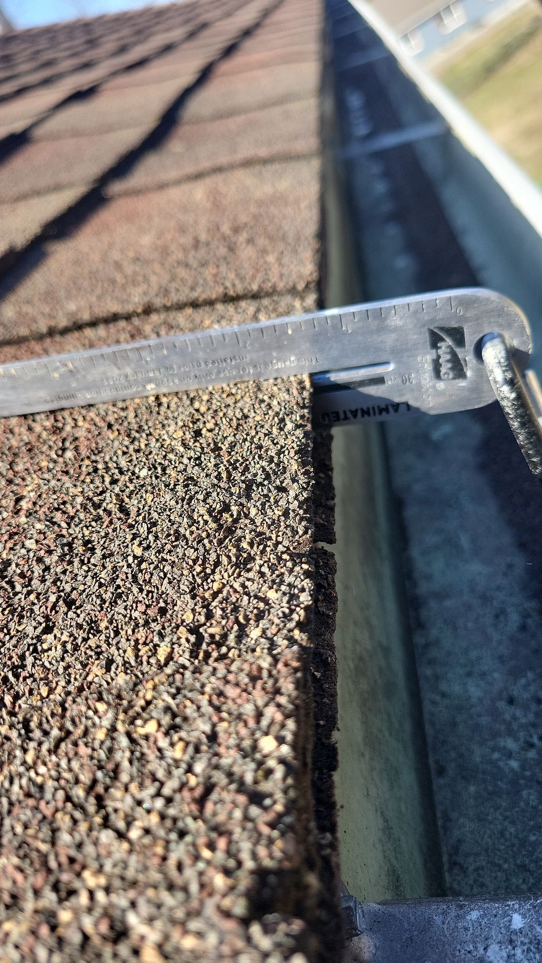 Close-up of a roof gutter with a metal tool resting on asphalt shingles and gravel debris