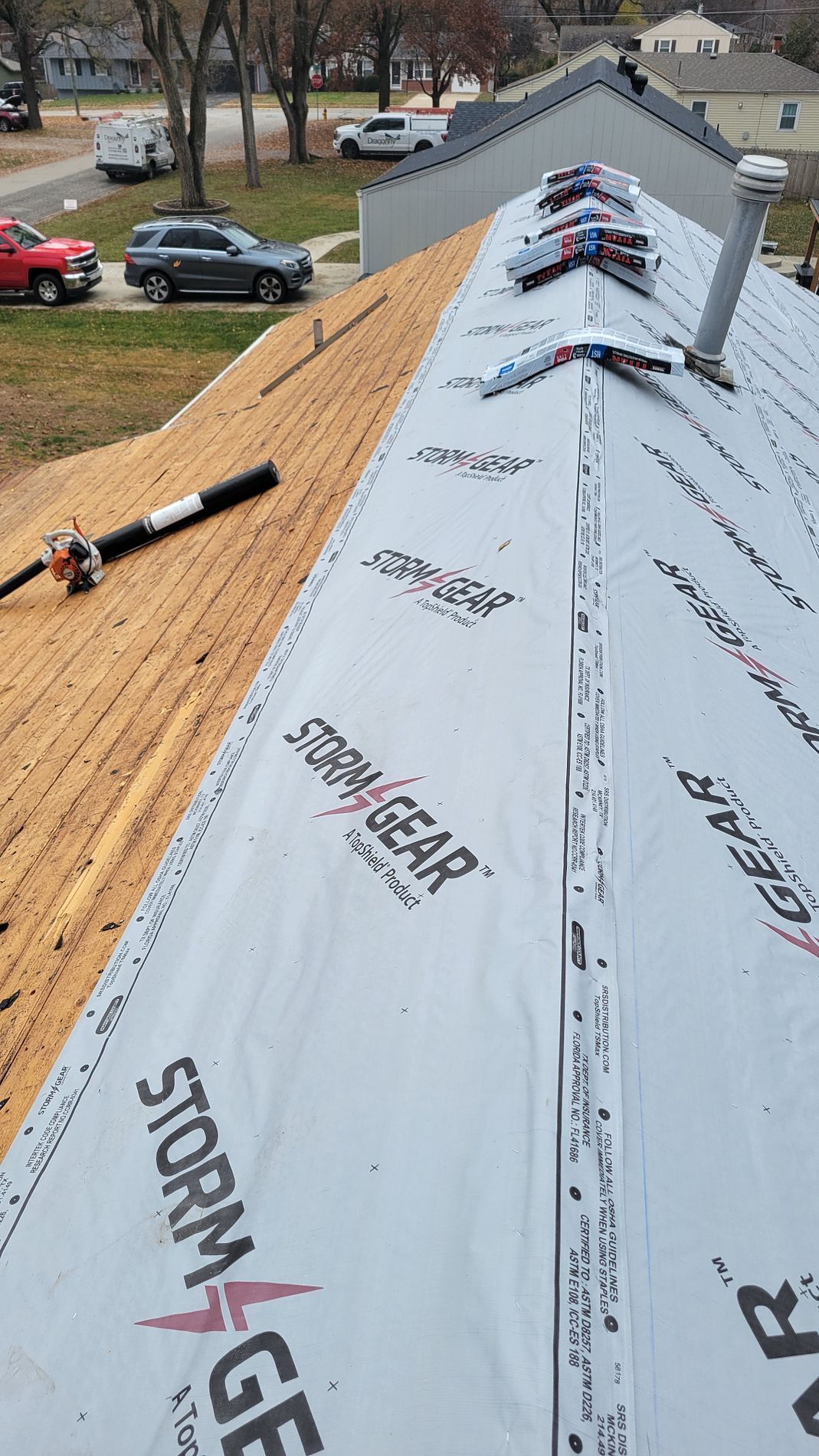 Roof under construction with white underlayment and exposed plywood, workers on the roof near a ridge vent.