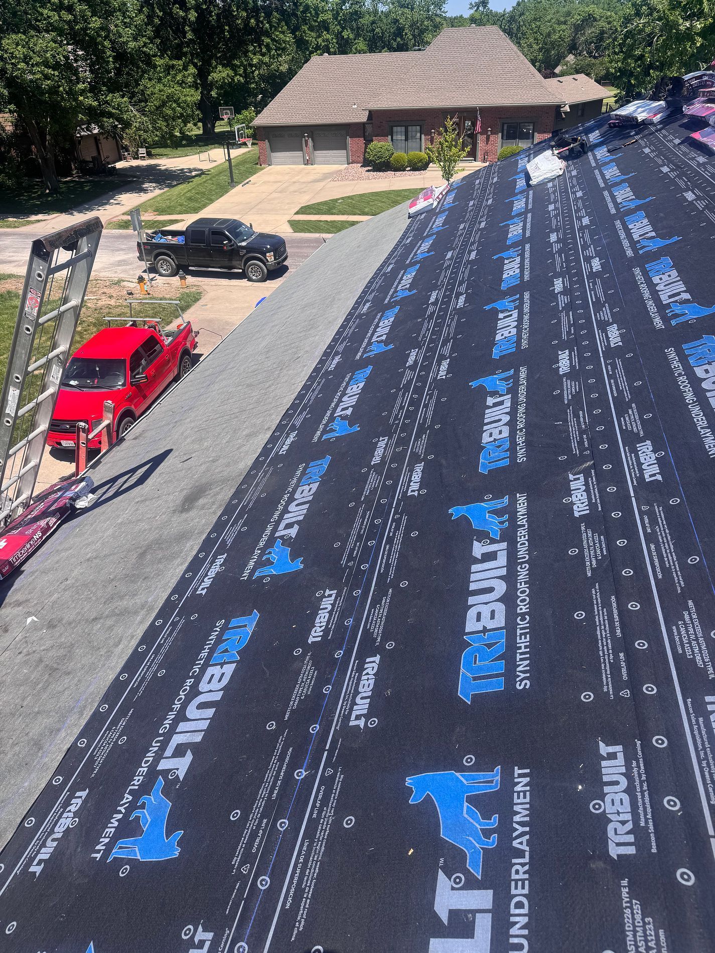 Roof under construction with black underlayment, a pickup truck, and trees beside a house
