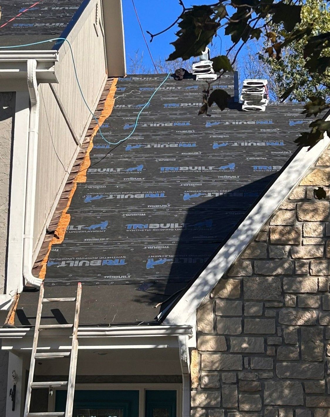 Roof under repair with black roofing underlayment and workers on a steep house roof
