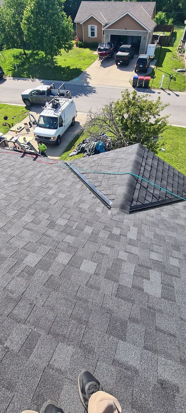 View from a roof over a suburban driveway with parked cars, green trees, and a house ahead