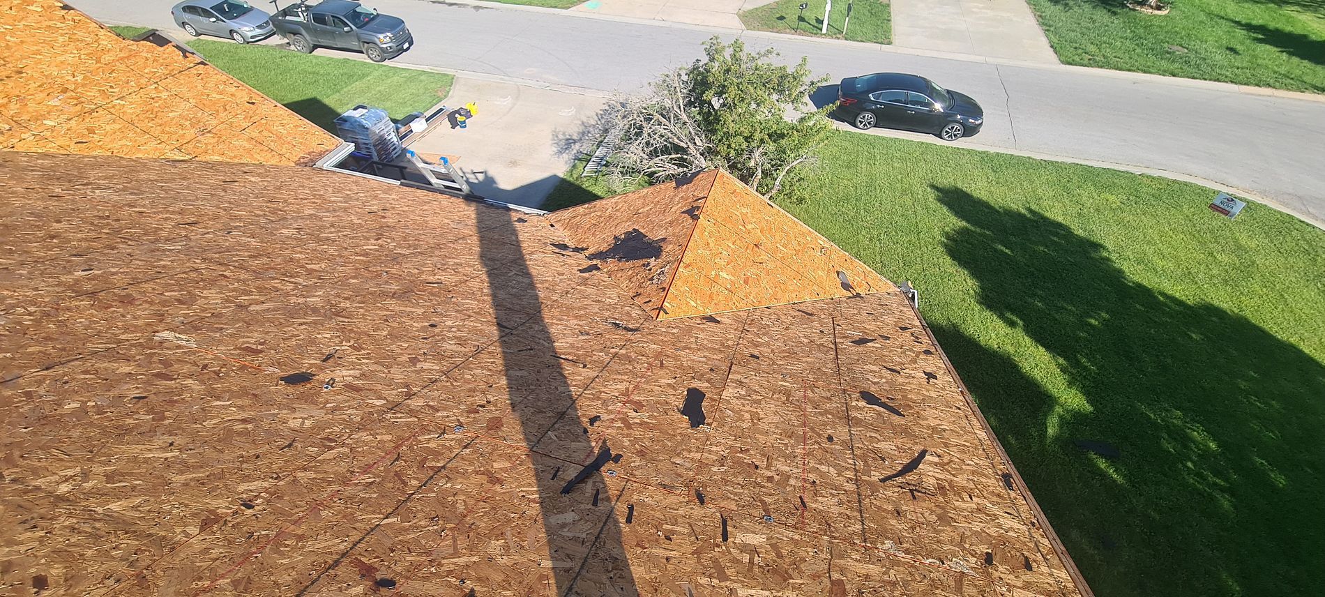 Brown roof shingles and solar panels overlooking a green lawn and street on a sunny day
