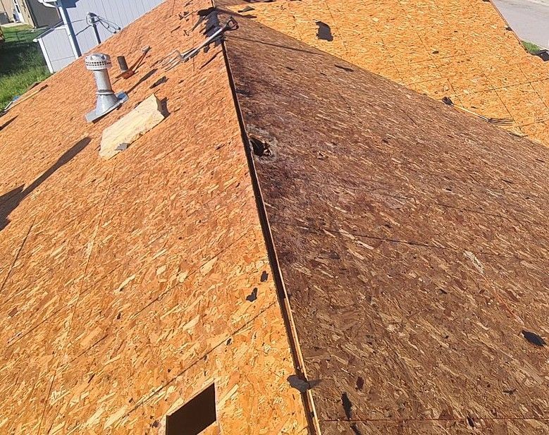 Roof with brown shingles and a steep ridge, viewed from above, with vents and a small skylight opening.