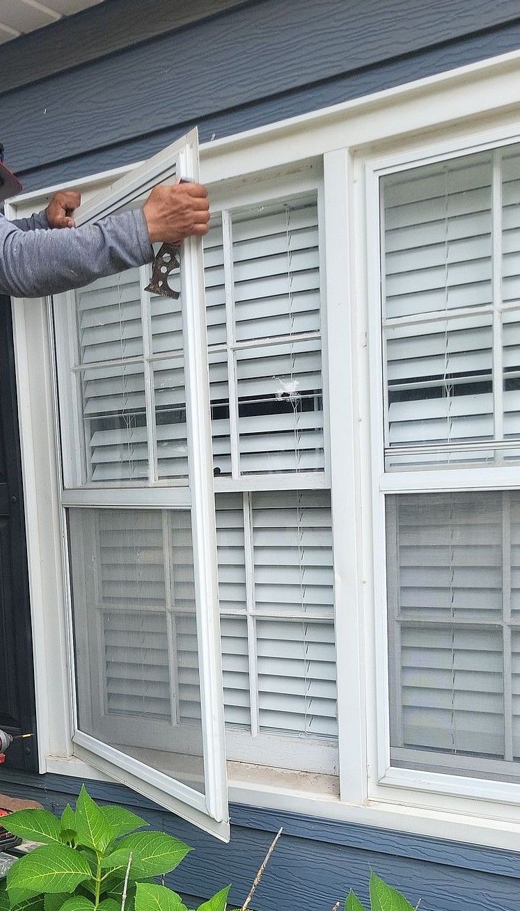 Person measuring a white window frame beside closed white blinds on a house exterior