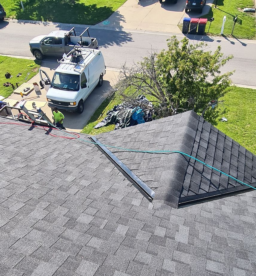 Roof repair crew and white truck working near a house with gray shingles and green lawn below.