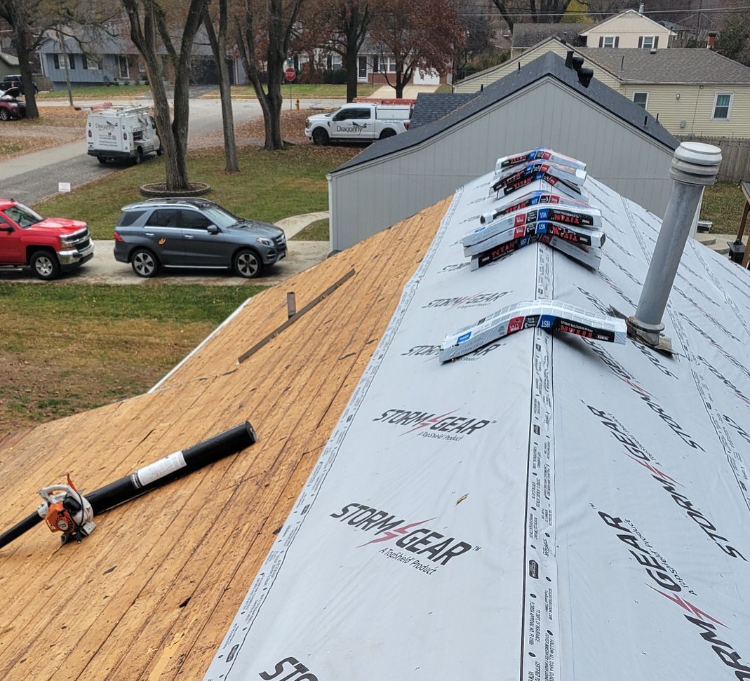 Roof under repair with plywood sheathing, white underlayment, and tools on a suburban home.