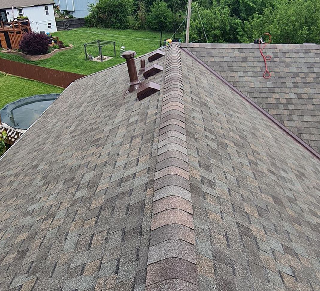 Rooftop with gray shingles and a vent pipe, overlooking a green backyard and neighboring house.