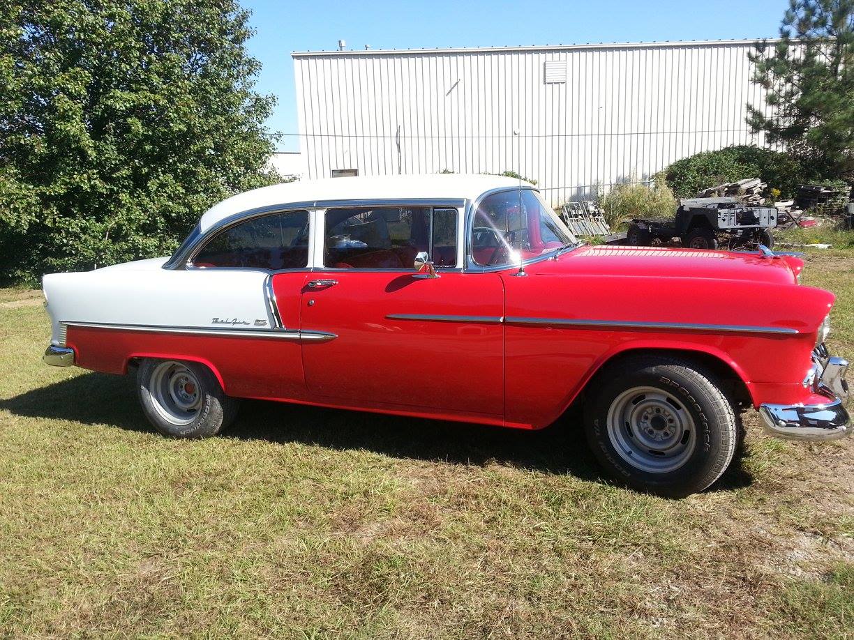 A red and white classic car is parked in a grassy field.
