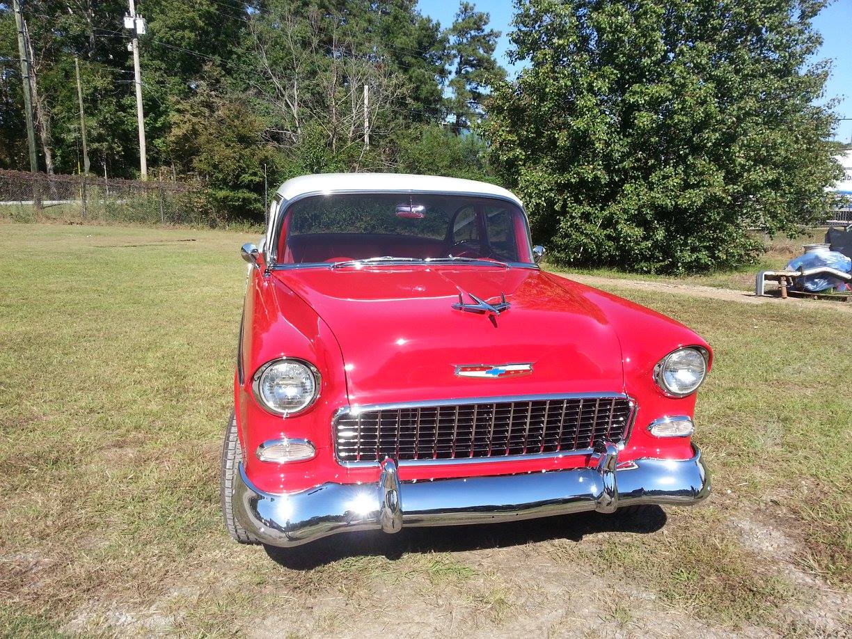 A red car with a white top is parked in a grassy field.