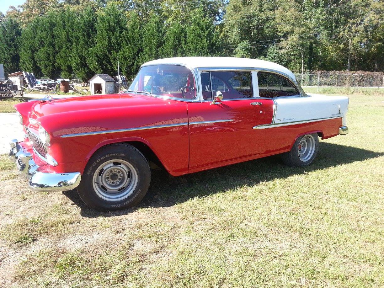 A red and white car is parked in a grassy field.