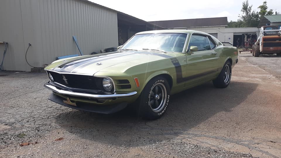 A green mustang is parked in a gravel lot in front of a building.