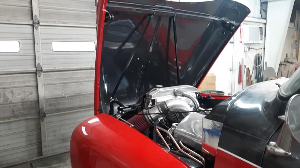 A red car with the hood up in a garage