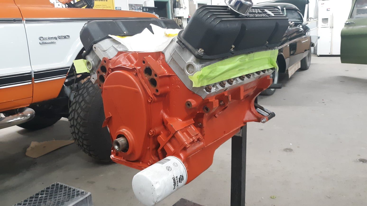 A red engine is sitting on a stand in a garage next to a car.