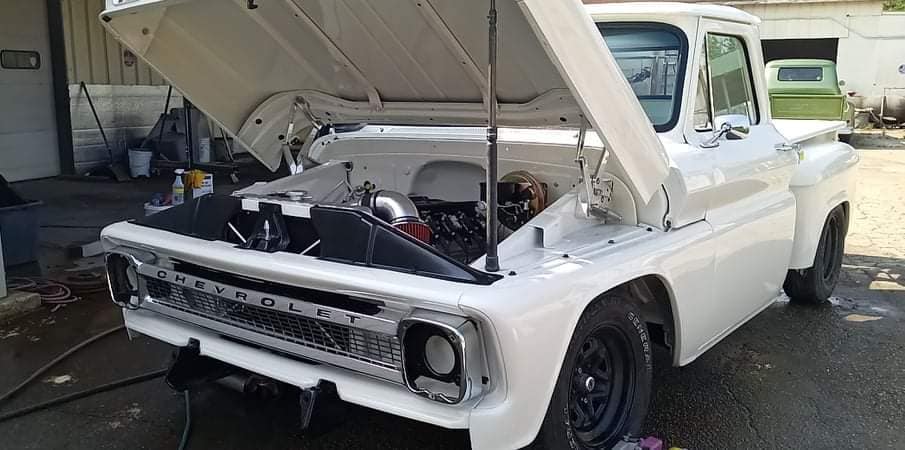 A white truck with the hood up is parked in a parking lot.