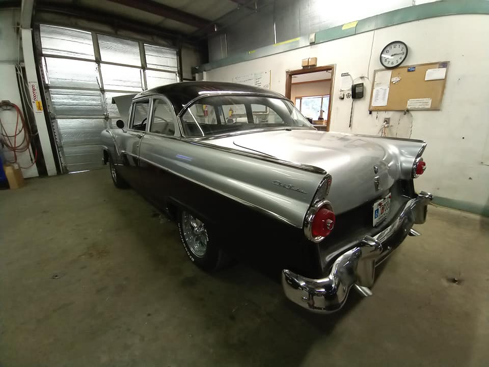 A black and silver car is parked in a garage with a clock on the wall.