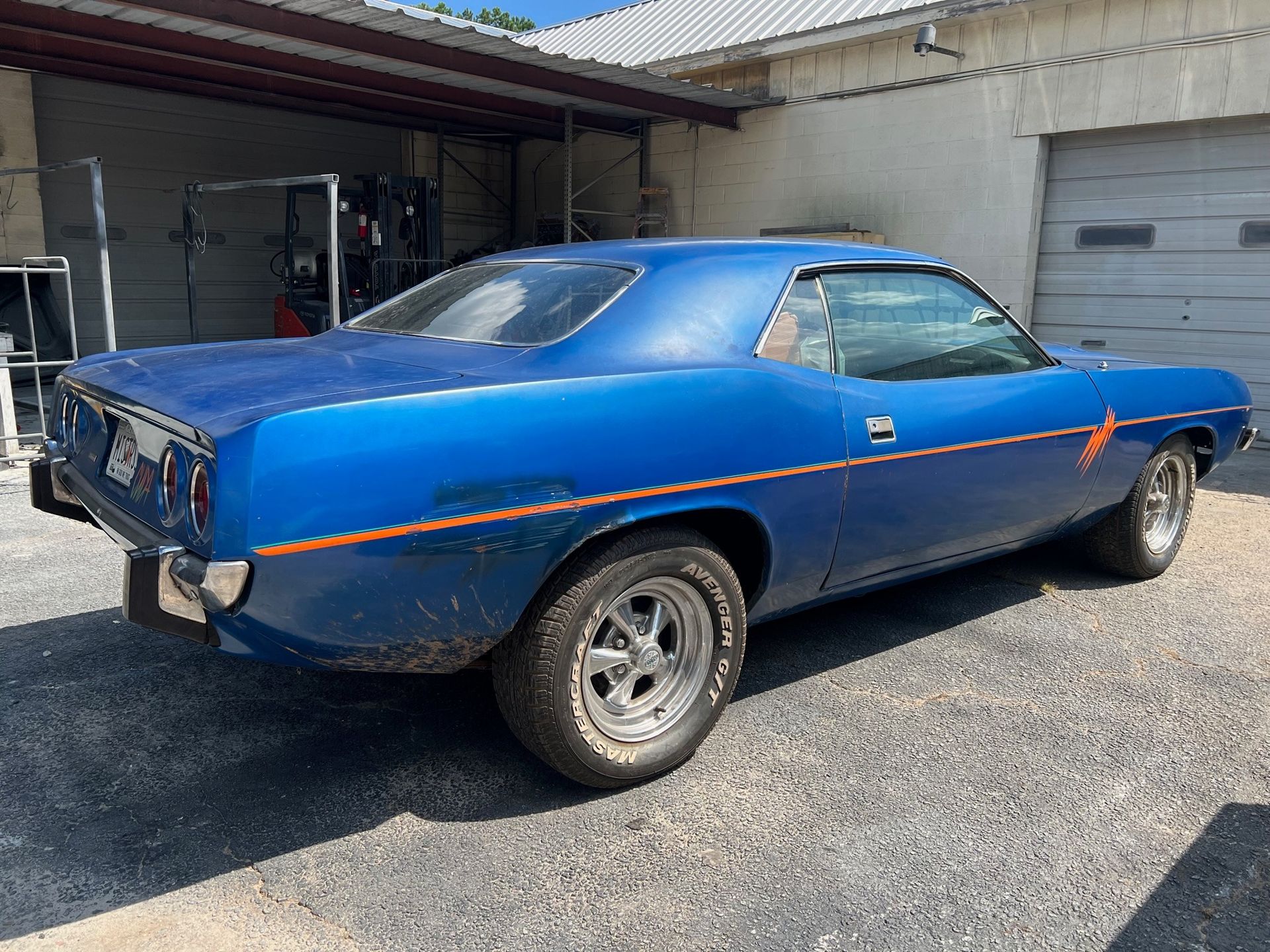 1973 Plymouth Barracuda is parked in front of a garage.