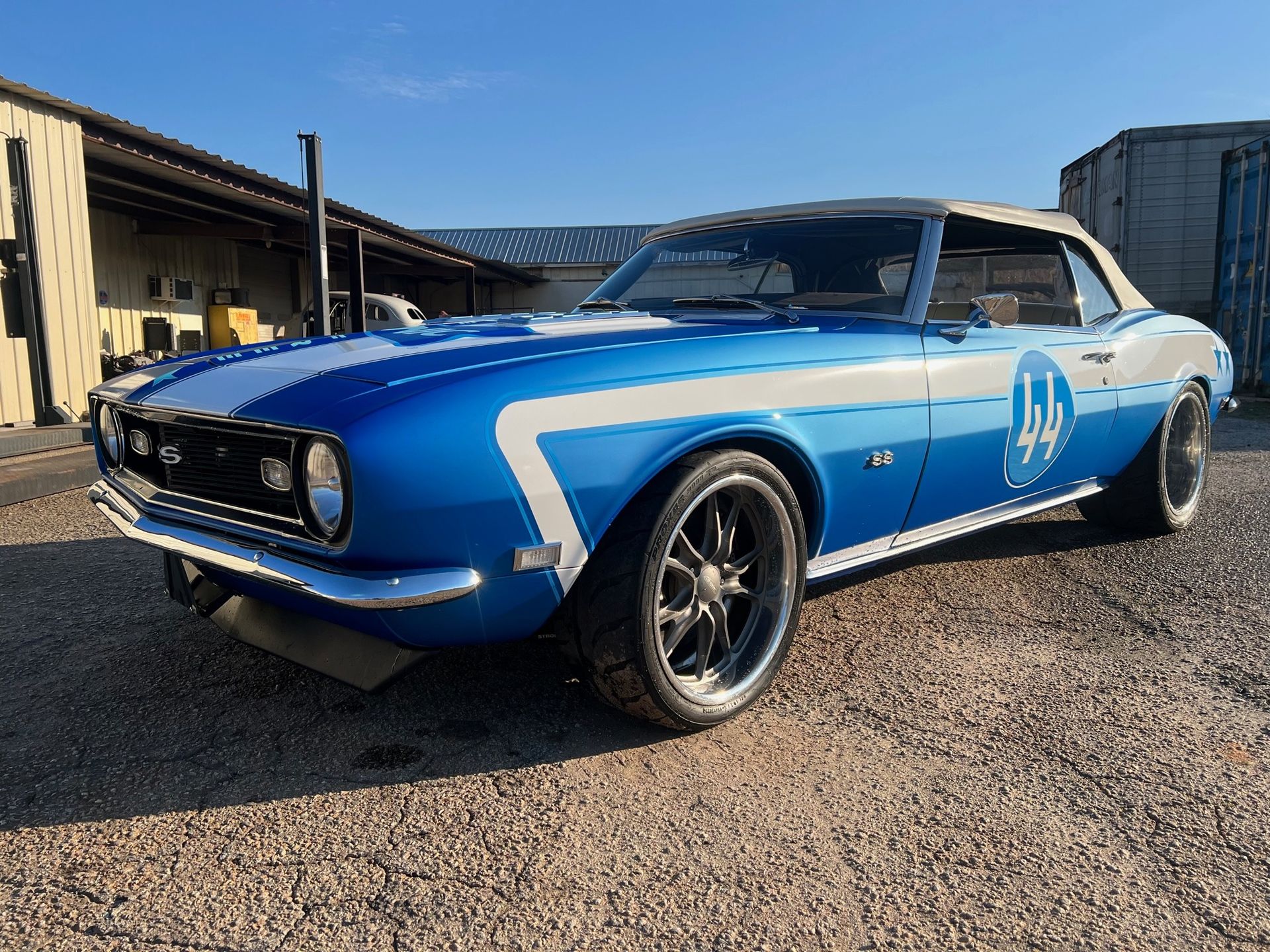 Blue convertible classic car with white racing stripes and number 44 parked outside.