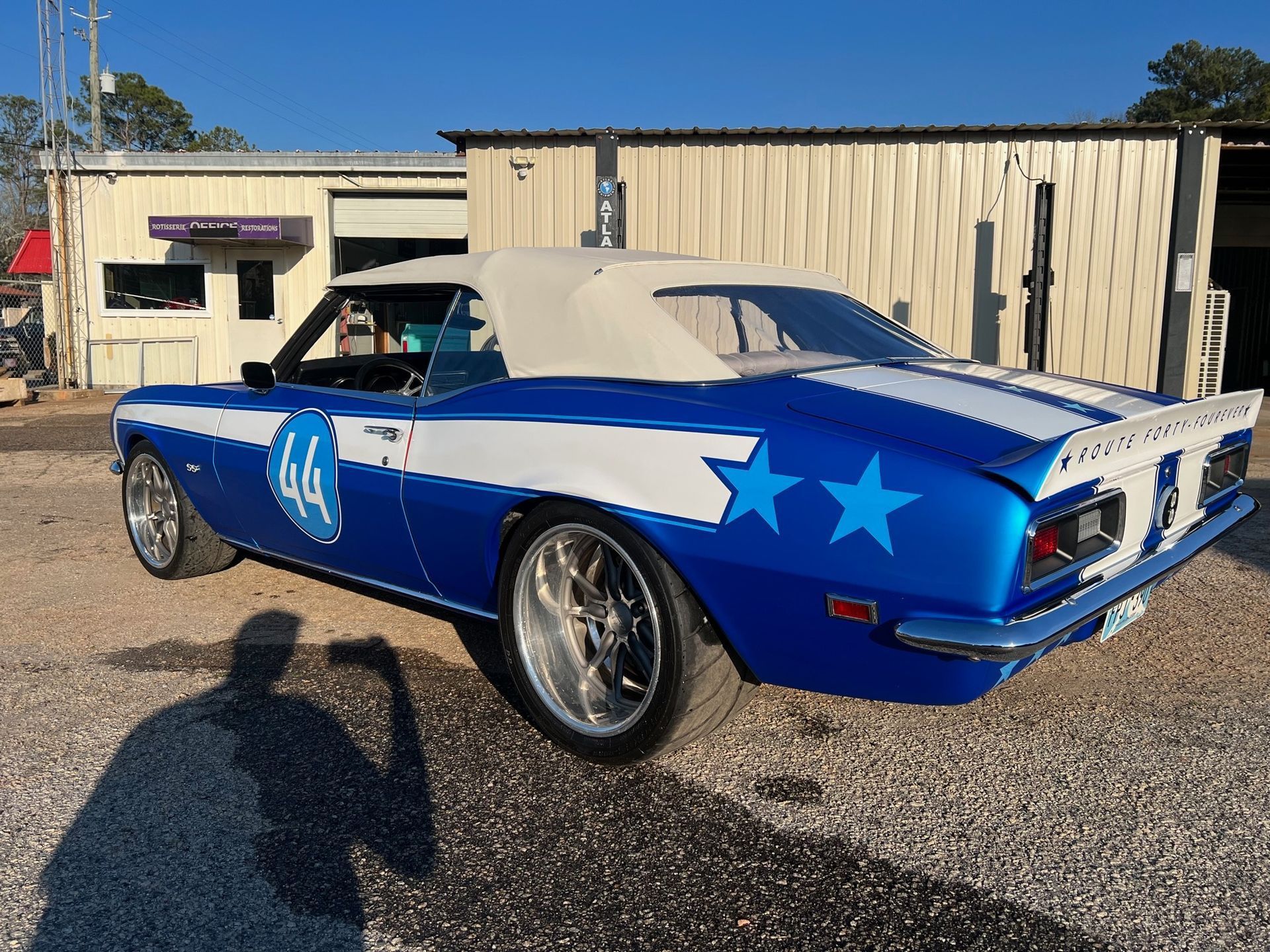 Blue and white custom convertible Camaro with stars and stripes, parked outside a building.