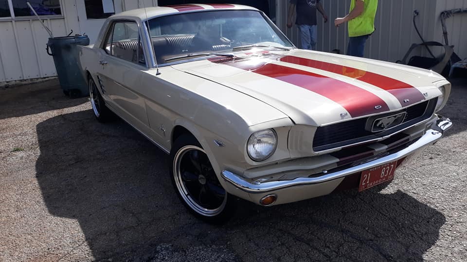 A white mustang with red stripes on the hood is parked in a parking lot.