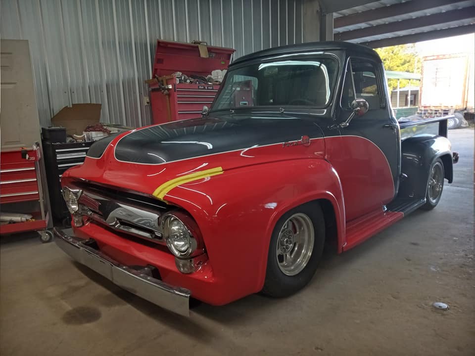 A red truck with a black hood is parked in a garage.